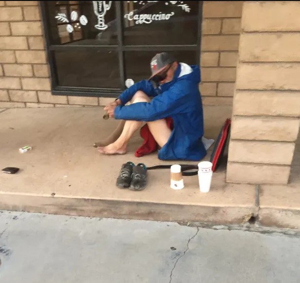 People experiencing homelessness as a homeless man sits in front of a business